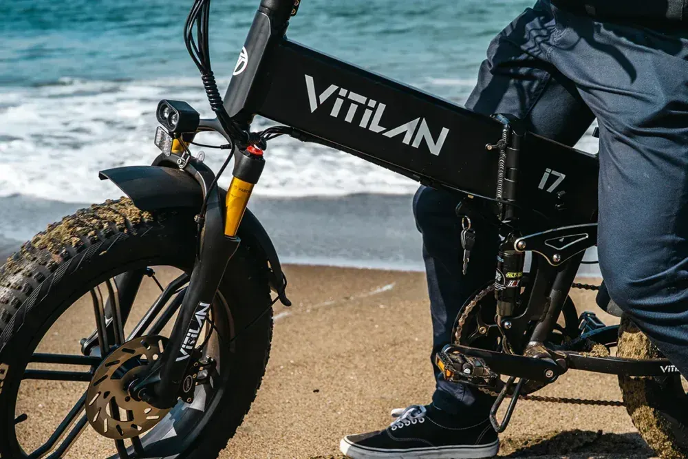 Vitilan I7 Pro en uso, ciclista en camino de tierra, luces LED encendidas y asiento ajustado.